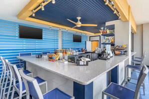 Eine Bar mit einer langen Theke, Barhocker, Deckenventilatoren und Regalen mit Flaschen.