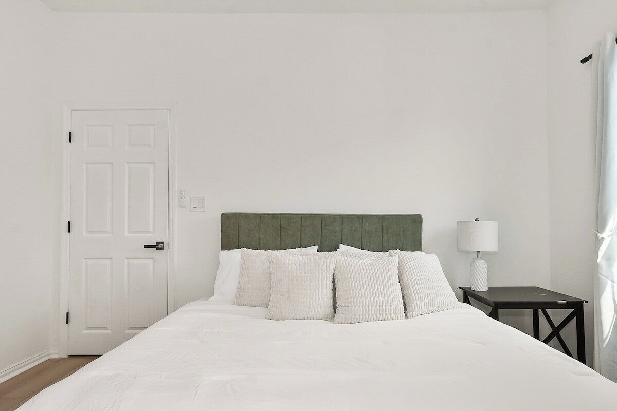 A hotel room with a bed, a nightstand, a lamp, and a door.