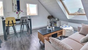 Camera da loft moderna con finestra sul tetto, zona pranzo con sedie, un divano e un tavolino con un vaso e candele.