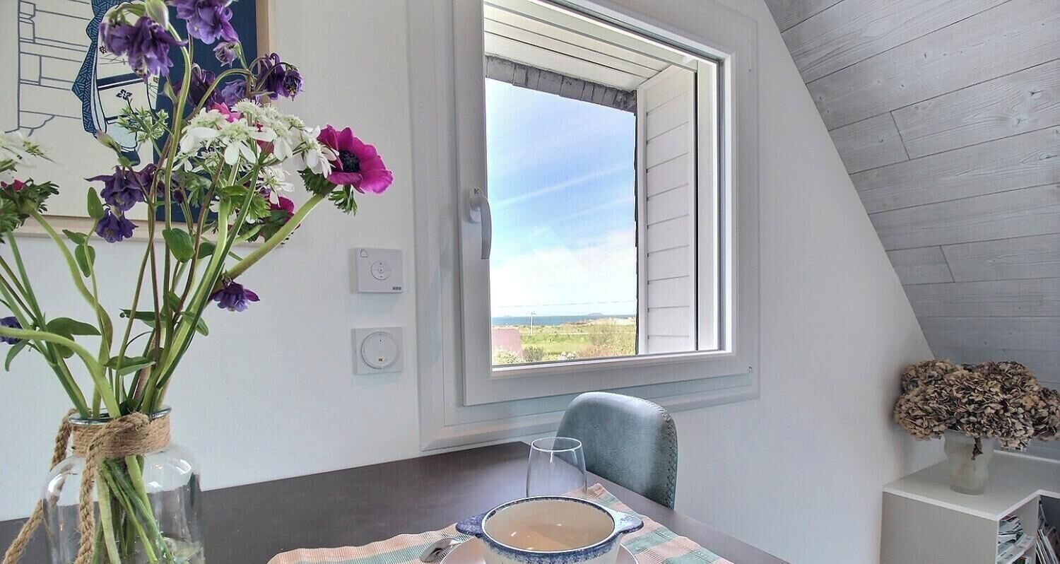 A dining area with a table, a vase of flowers, a window with a view, and a chair.