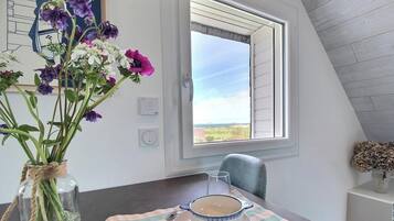 A dining area with a table, a vase of flowers, a window with a view, and a chair.
