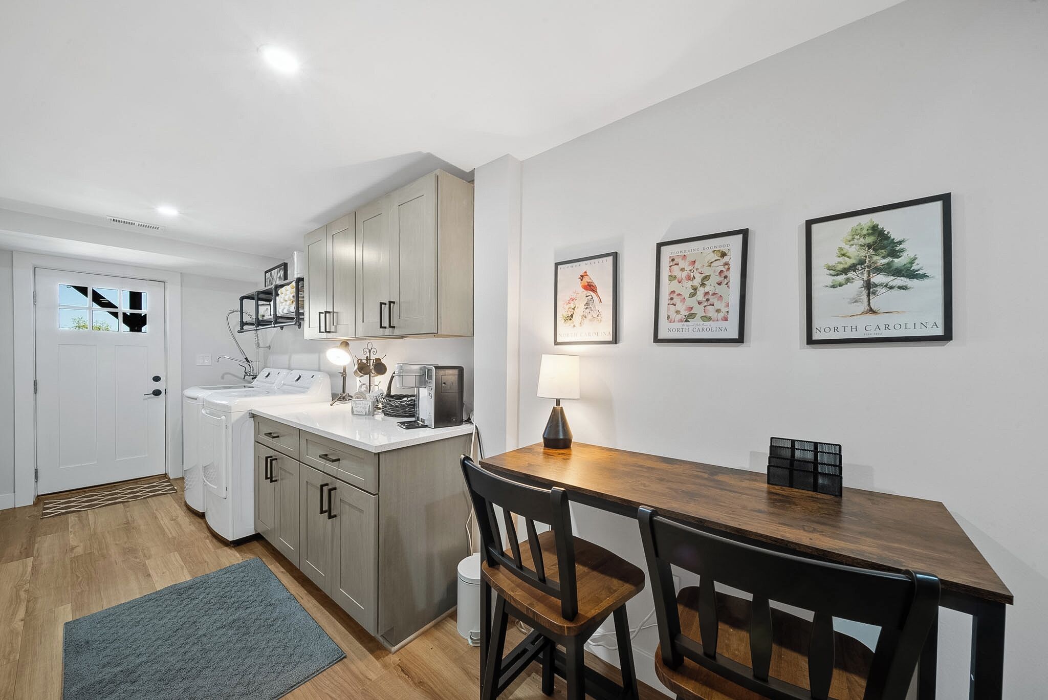 A modern kitchen with white cabinets, a wooden dining table, and a gray rug.
