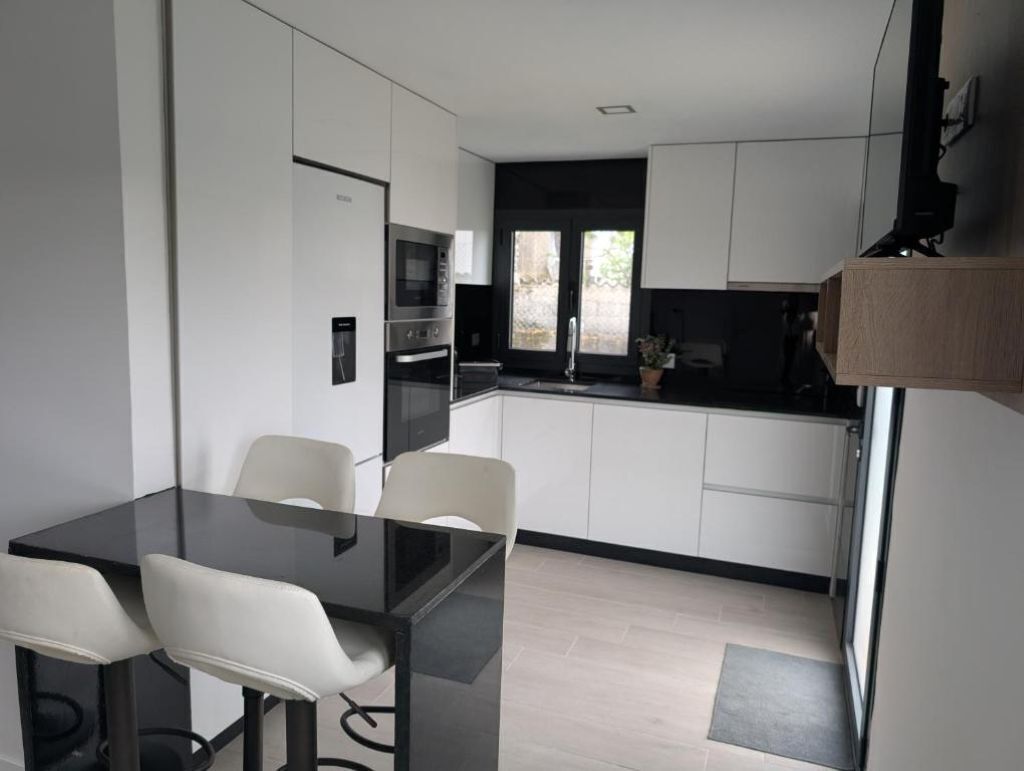 A modern kitchen with a dining area, featuring a black table, white chairs, and a built-in oven.
