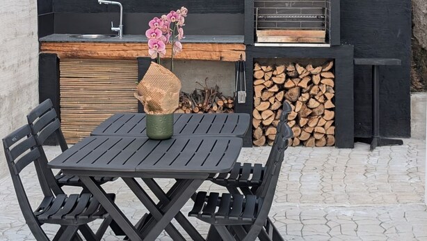 Een buitenkeuken met een barbecue, een spoelbak en een tafel met stoelen.