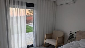 Een slaapkamer met een bed, een stoel, een raam met dunne gordijnen en een airconditioning.