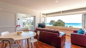 A modern living room with a dining area, a sofa, and a TV. - Vista On The Beach at The Sands (Waiheke Island)