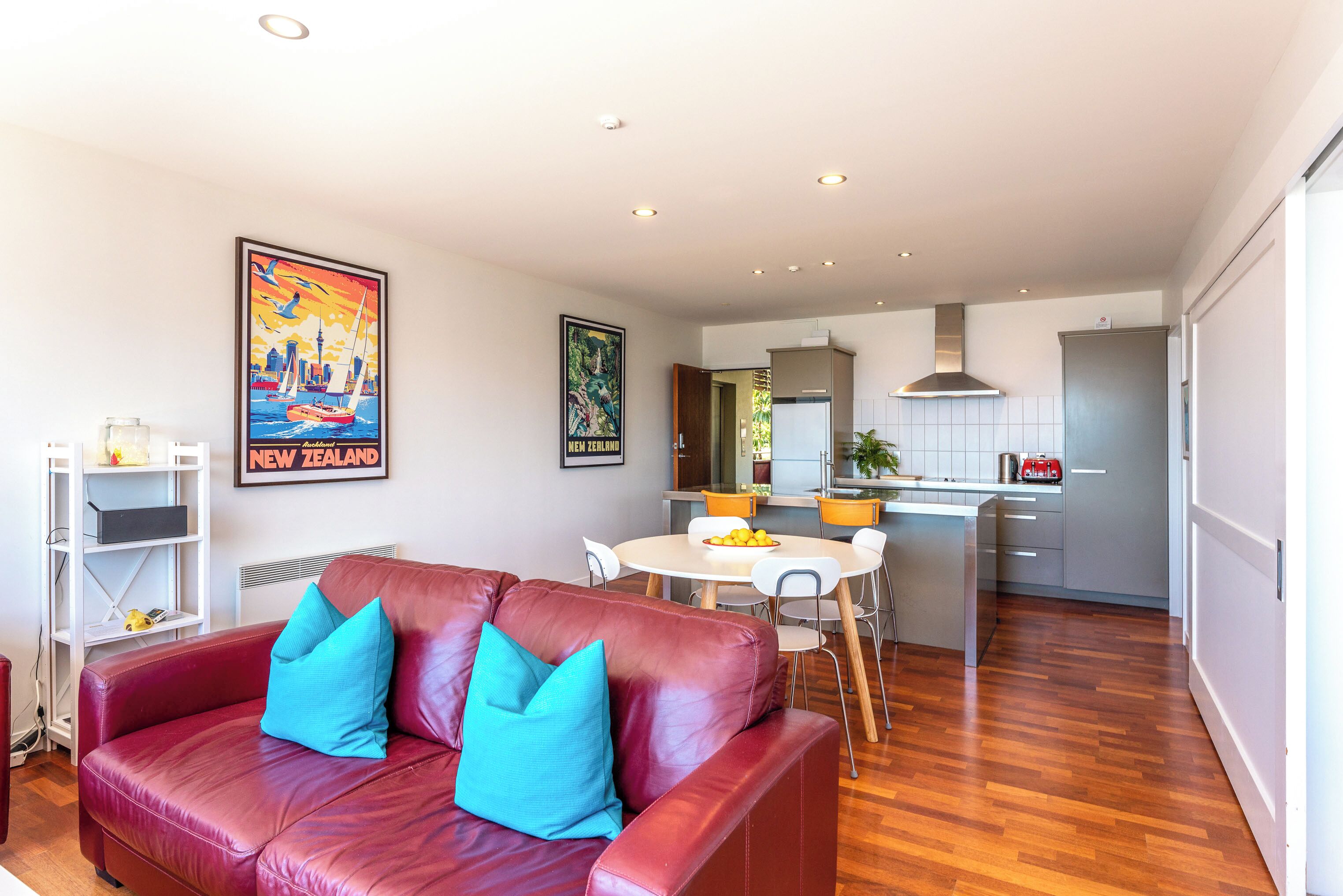 A modern living room with a red leather sofa, a dining area with a white table, and a kitchen in the background.