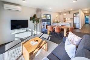Ein modernes Wohnzimmer mit Flachbildfernseher, Couchtisch, Sofa und Essbereich mit Stühlen und Tisch.