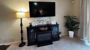 A living room with a flat-screen TV mounted on the wall, a lamp, a console table with decorative items, and a potted plant. - 2-bedroom 2-bath condo in lovely Mishawaka close to Notre Dame. (Mishawaka)