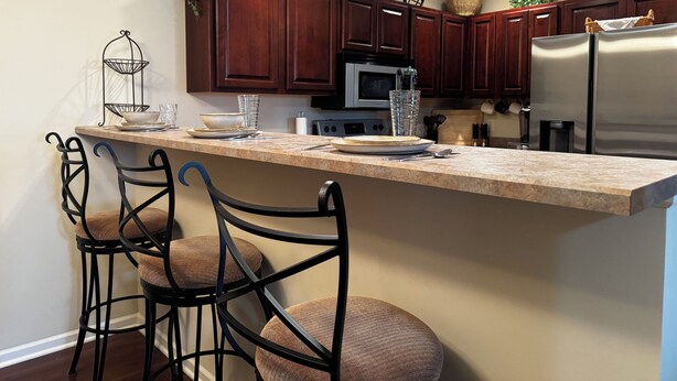 A kitchen with a bar area, wooden cabinets, stainless steel appliances, and a sign that says 'BE OUR GUEST'. - 2-bedroom 2-bath condo in lovely Mishawaka close to Notre Dame. (Mishawaka)