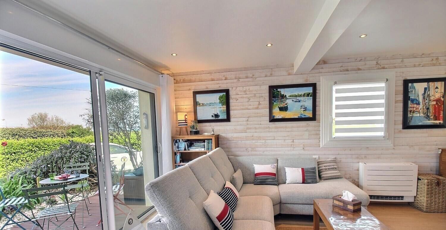 A modern living room with a large window, a sofa, a table, and a bookshelf.