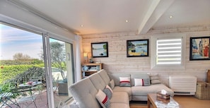 A modern living room with a large window, a sofa, a table, and a bookshelf. - Ty Royau'M-Maison - TREVOU TREGUIGNEC (TREVOU TREGUIGNEC)