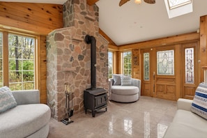 Una habitación acogedora con chimenea de piedra, paredes de madera y ventanas amplias.