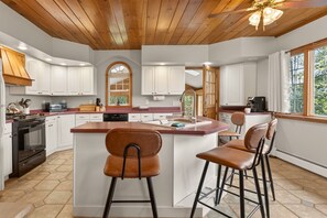 Una cocina con armarios blancos, una isla central con taburetes, una estufa y un lavabo.