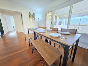 Un espace repas avec une table en bois dressée pour quatre personnes, des bancs et une vue dégagée grâce à de grandes fenêtres.