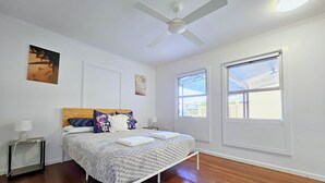 A bedroom with a bed, a ceiling fan, two windows, and artwork on the walls. - SeaBreeze Retreat@BaySide/Clevelnd/Brisbne/GoldCst (Cleveland)