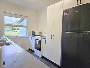 Een keuken met witte kastjes, een zwarte koelkast, een magnetron en een fornuis.