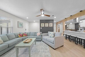 A modern living room with a sectional sofa, a coffee table, and a kitchen area with bar stools. - Sleeps Ten, Pet friendly, White sand beaches (Pensacola)