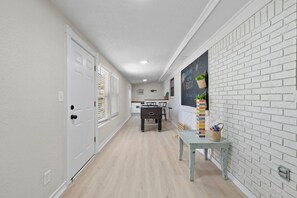 A hallway with white brick walls, a light wooden floor, a door with a window, and a small table with a plant and a basket. - Sleeps Ten, Pet friendly, White sand beaches (Pensacola)