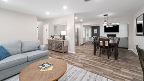Una sala de estar moderna con un sofá gris, una mesa de centro de madera y una zona de comedor con una mesa y sillas de madera oscura.