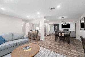 A modern living room with a grey sofa, wooden coffee table, and a dining area with a dark wooden table and chairs. - Sea`s the Day Getaway (Pensacola)