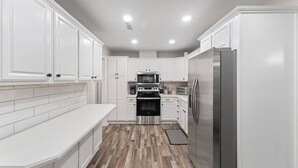 Una cocina moderna con armarios blancos, electrodomésticos de acero inoxidable y suelo de madera en patrón de espiga.