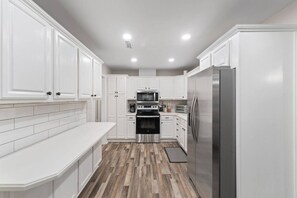A modern kitchen with white cabinetry, stainless steel appliances, and a herringbone wood floor. - Sea`s the Day Getaway (Pensacola)