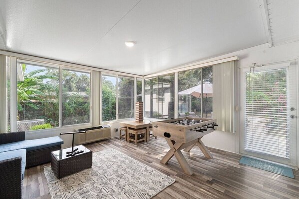 A spacious room with large windows, a foosball table, a sofa, and a small table. - Sea`s the Day Getaway (Pensacola)