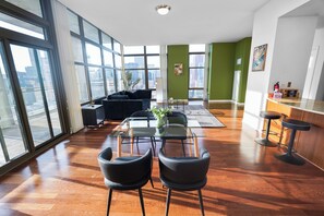 Un salón amplio con una mesa de vidrio, sillas negras, un sofá y vistas de la ciudad a través de amplias ventanas.