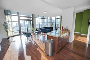 Eine moderne Küche mit einer großen Kochinsel, einem Essbereich mit Stühlen und Blick auf die Stadt durch große Fenster.