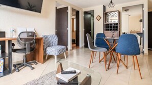 Una sala de estar moderna con una mesa de centro de vidrio, un escritorio con una computadora y un comedor con sillas.
