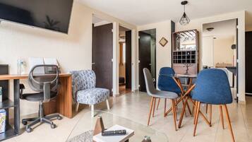 A modern living room with a glass coffee table, a desk with a computer, and a dining area with chairs.