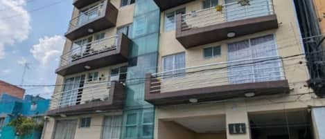 A multi-story residential building with balconies, a gated entrance, and a visible staircase leading to the entrance.