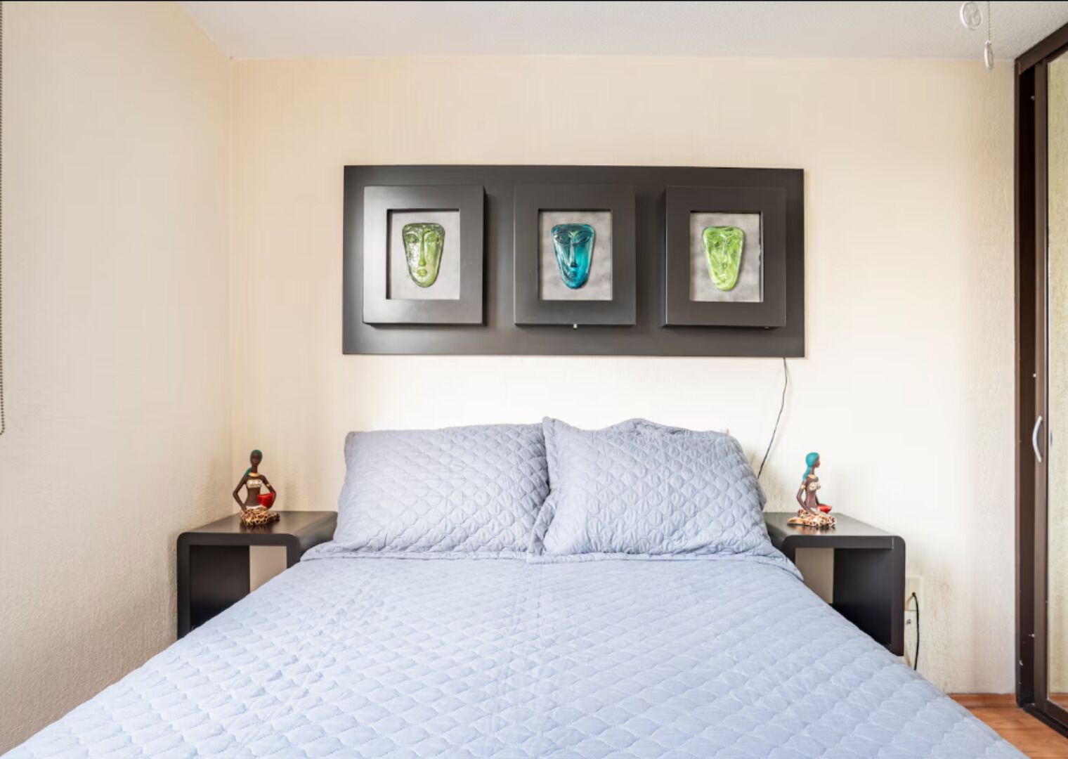 A bedroom with a bed, two nightstands, and three framed artworks on the wall.