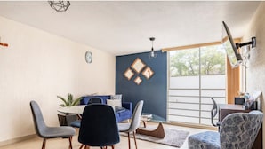 Una sala de estar moderna con comedor, un sofá azul, una mesa de centro y un ventanal con vistas.