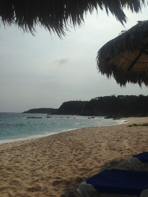 Una playa con una sombrilla de paja y sillones de descanso.