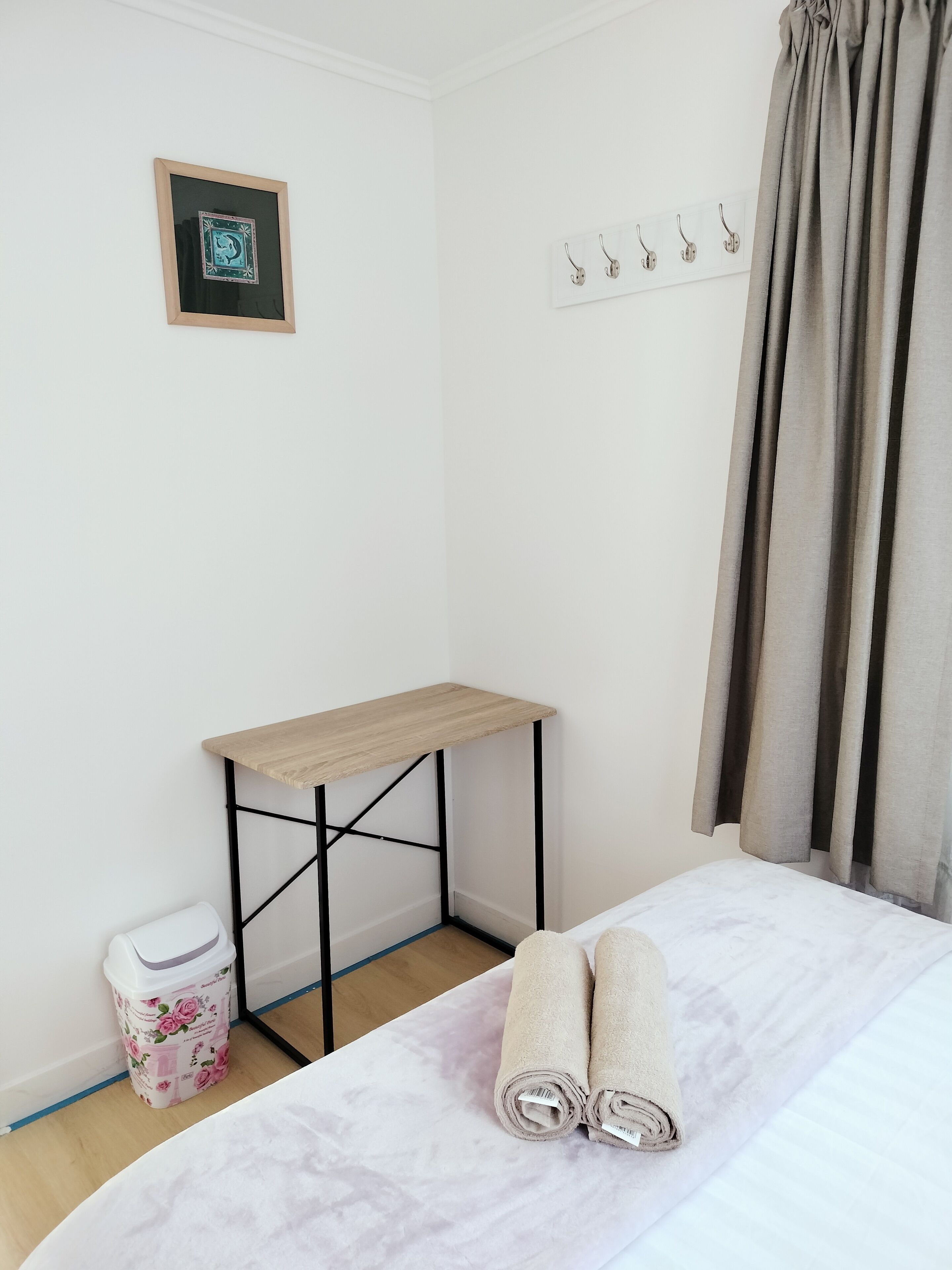 Un lit bien fait, avec des serviettes pliées, une petite table en bois, une poubelle et un interrupteur fixé au mur.