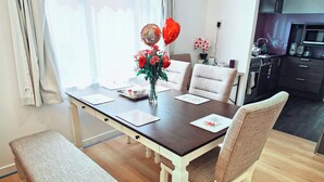 A dining area with a wooden table, four chairs, a bench, a vase with flowers, and a window with curtains. - Cozy 4 bedrooms House BNB at Whangarei Town center. Next to supermarket/ schools (Whangārei)