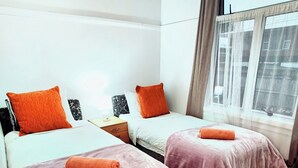 A room with two beds, each with a pink bedspread and an orange pillow. There is a wooden nightstand with a lamp between the beds. - Cozy 4 bedrooms House BNB at Whangarei Town center. Next to supermarket/ schools (Whangārei)
