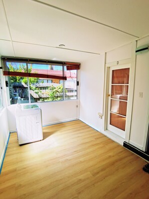Een kamer met houten vloer, een radiator, een raam met zonwering en een deur met een raampje.