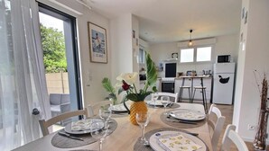 Zona pranzo con tavolo apparecchiato per quattro, cucina sullo sfondo e porta che dà su uno spazio esterno.
