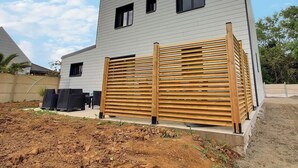 Un edificio moderno a due piani con facciata grigia, una recinzione in legno e un patio arredato.