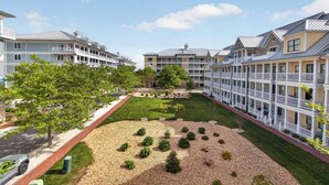 A multi-story hotel with balconies, a central courtyard with a lawn and trees, and a gravel area with shrubs. - 6 Sunset Island Drive 3F (Ocean City)
