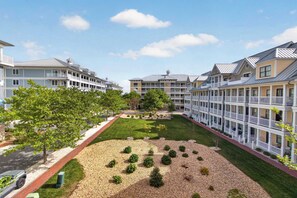 A multi-story hotel with balconies, a central courtyard with a lawn and trees, and a gravel area with shrubs. - 6 Sunset Island Drive 3F (Ocean City)
