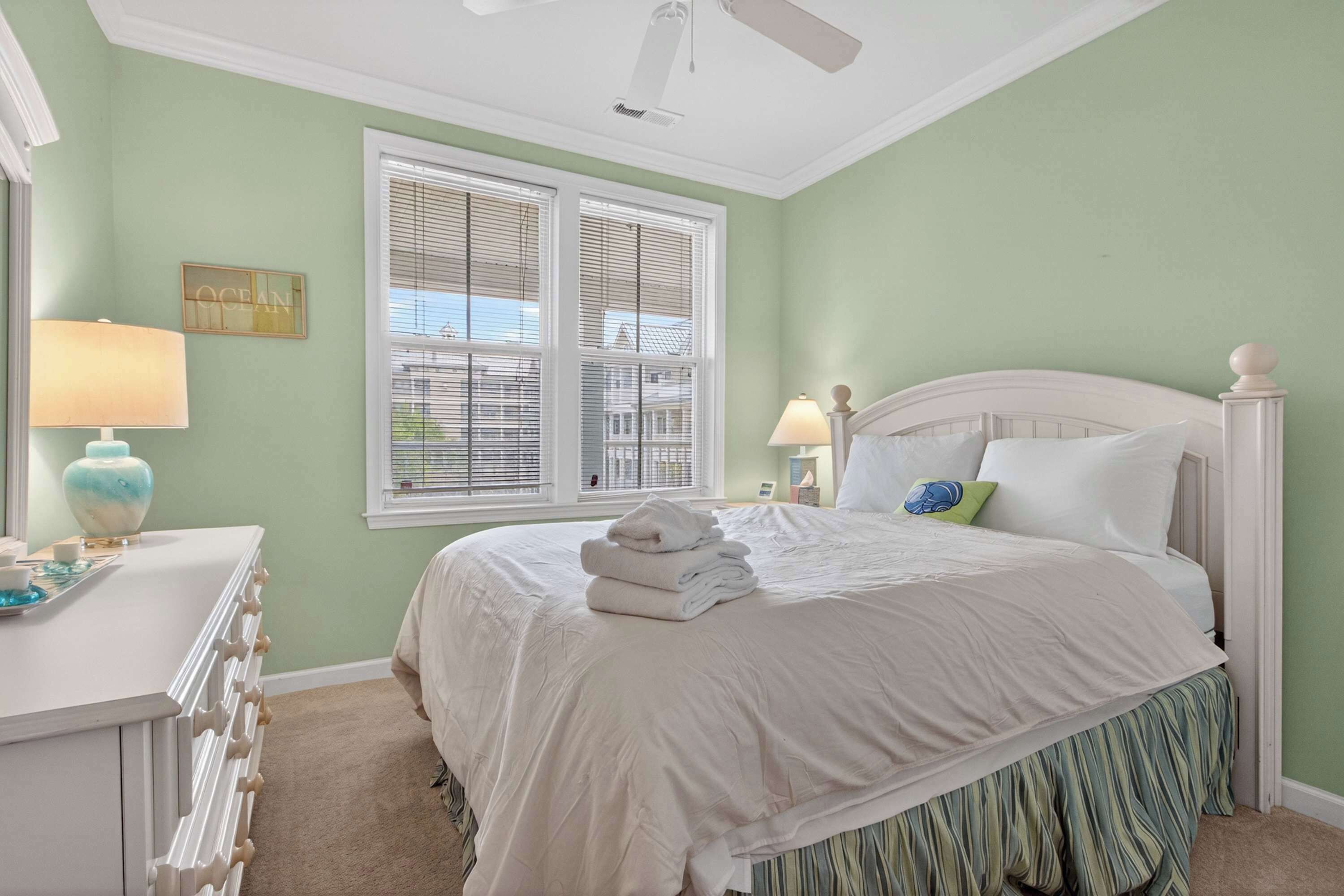A bedroom with a bed, a dresser, a window with blinds, and a ceiling fan.