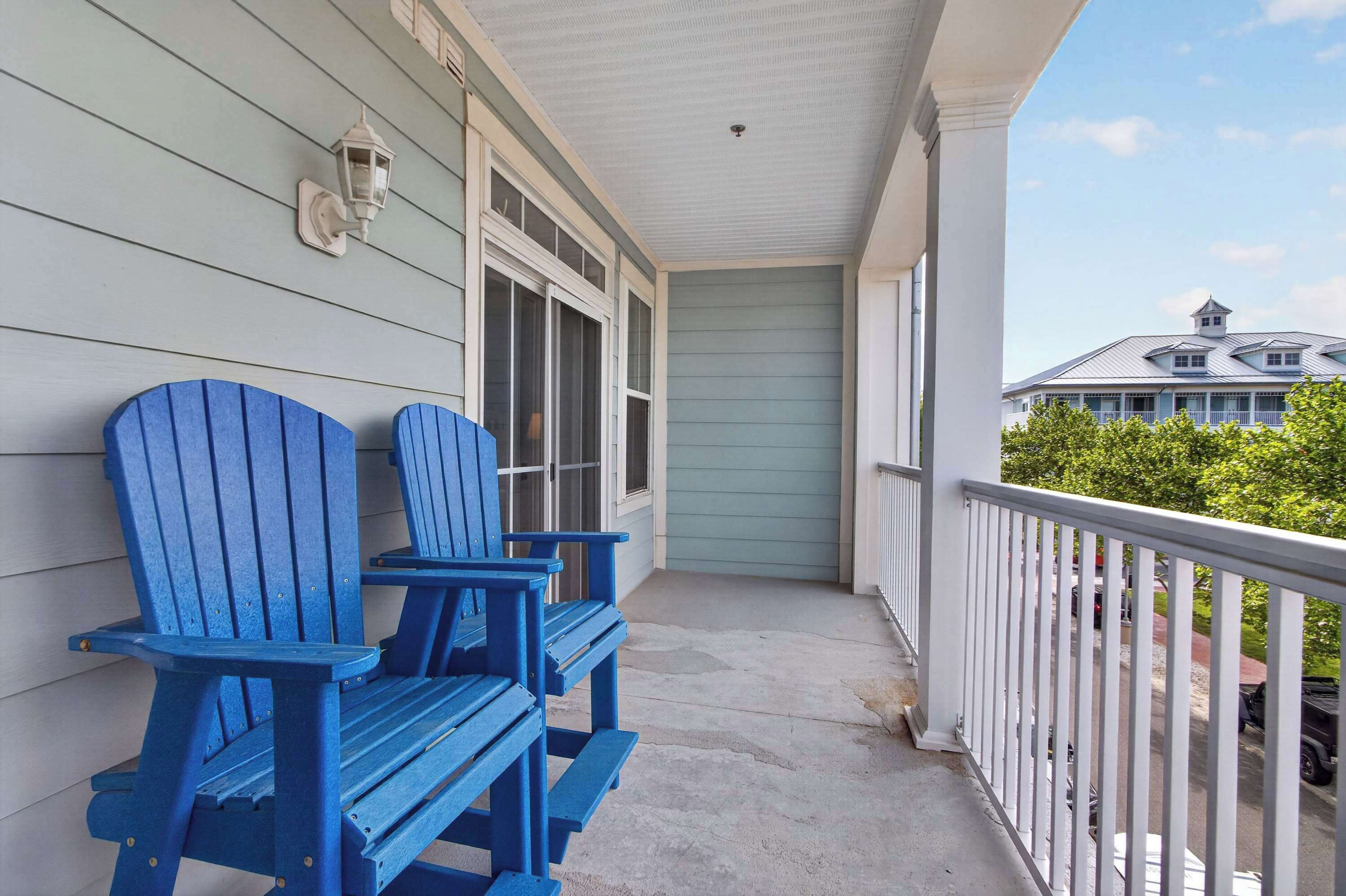 A porch with two Adirondack chairs, a white railing, and a view of a house in the background.