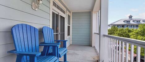 A porch with two Adirondack chairs, a white railing, and a view of a house in the background.