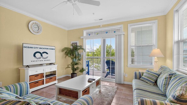 A living room with a sofa, a coffee table, a TV, a plant, and a balcony with a view. - 6 Sunset Island Drive 3F (Ocean City)