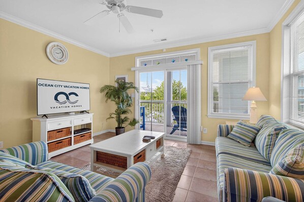 A living room with a sofa, a coffee table, a TV, a plant, and a balcony with a view. - 6 Sunset Island Drive 3F (Ocean City)