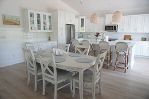 Eine moderne Küche mit weißen Schränken, einem Essbereich mit Holztisch und -stühlen sowie einer zentralen Kochinsel mit Sitzgelegenheiten.